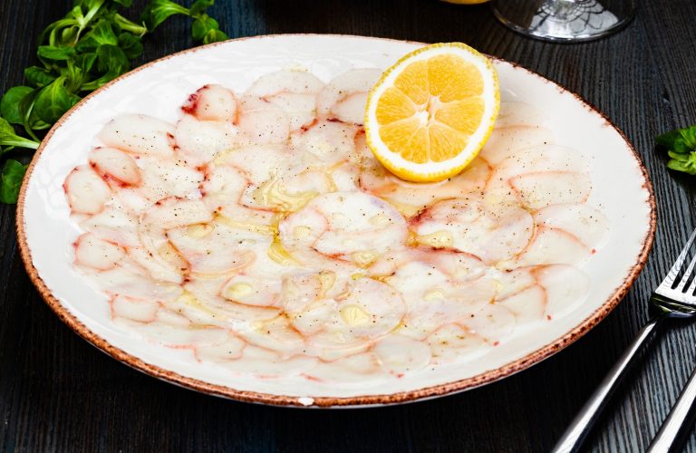 Octopus carpaccio with lemon on white plate. - delicious